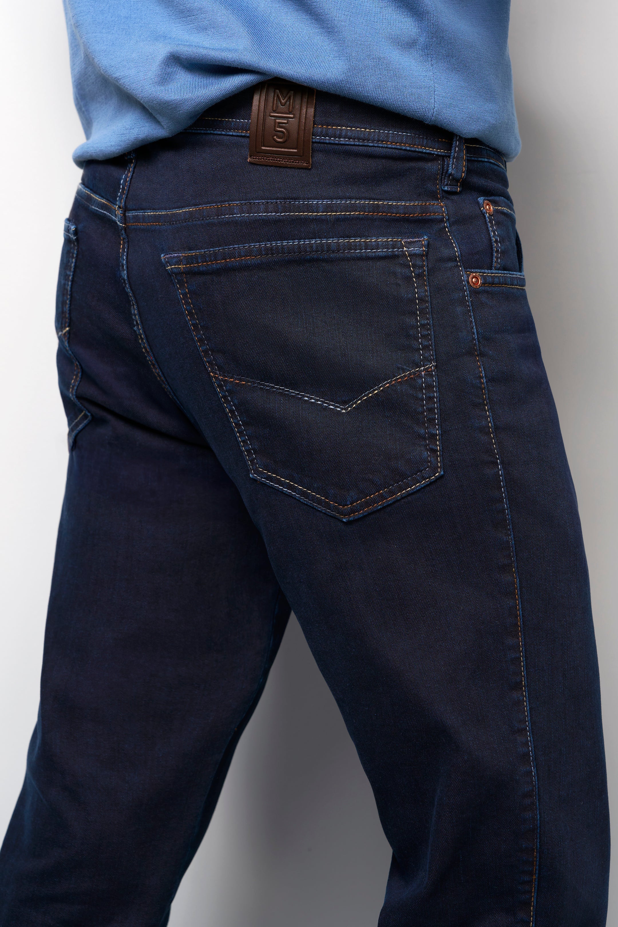 Dark blue jeans worn by a person on a plain background